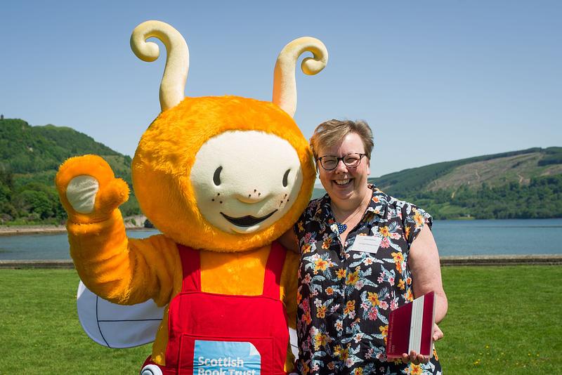 A smiling woman with short hair has her arm around a human-sized mascot of the Bookbug 
